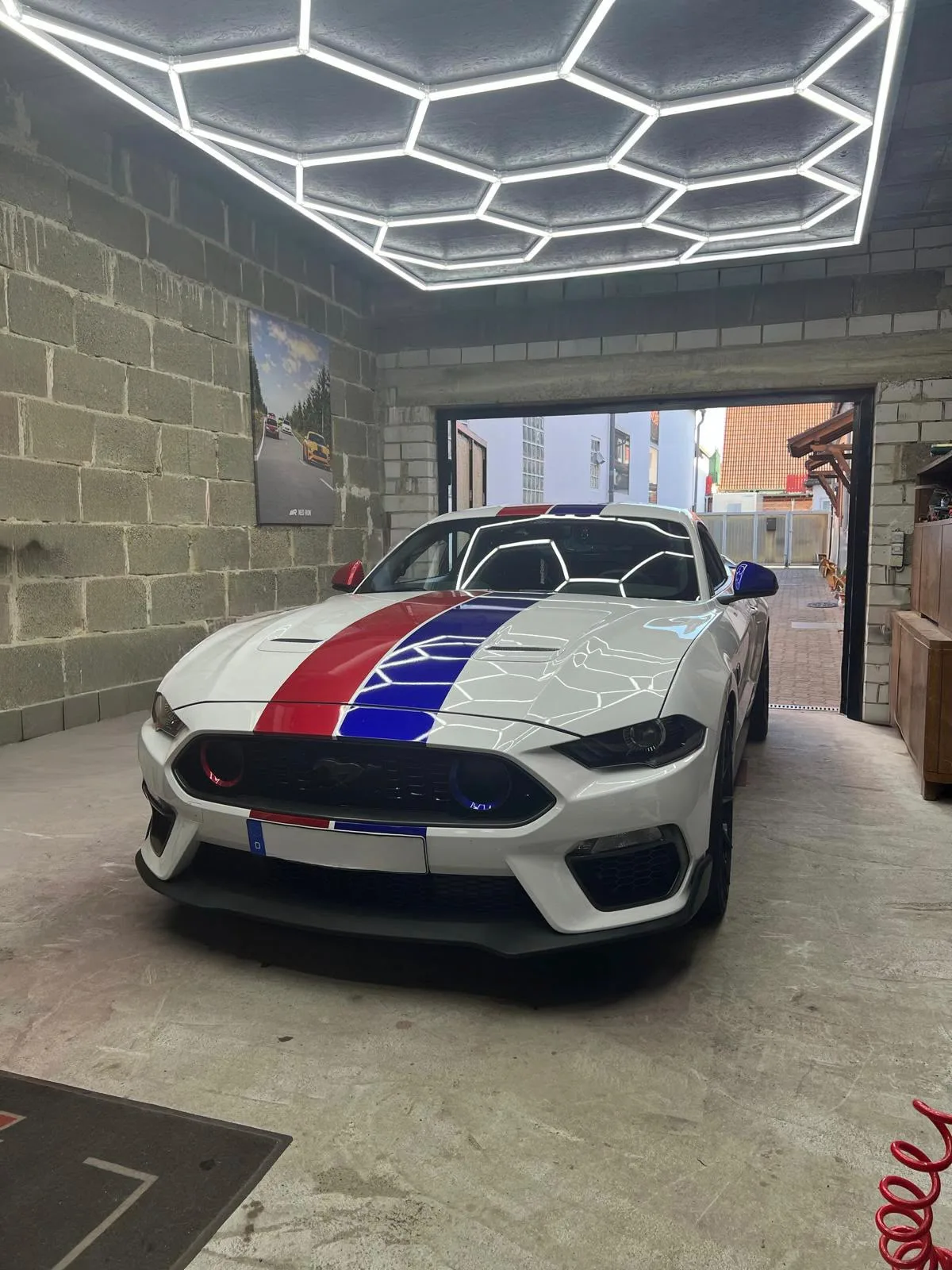 Weißer Ford Mustang Mach 1 mit roten und blauen Rennstreifen unter der LED-Wabenbeleuchtung bei LMT-Customz