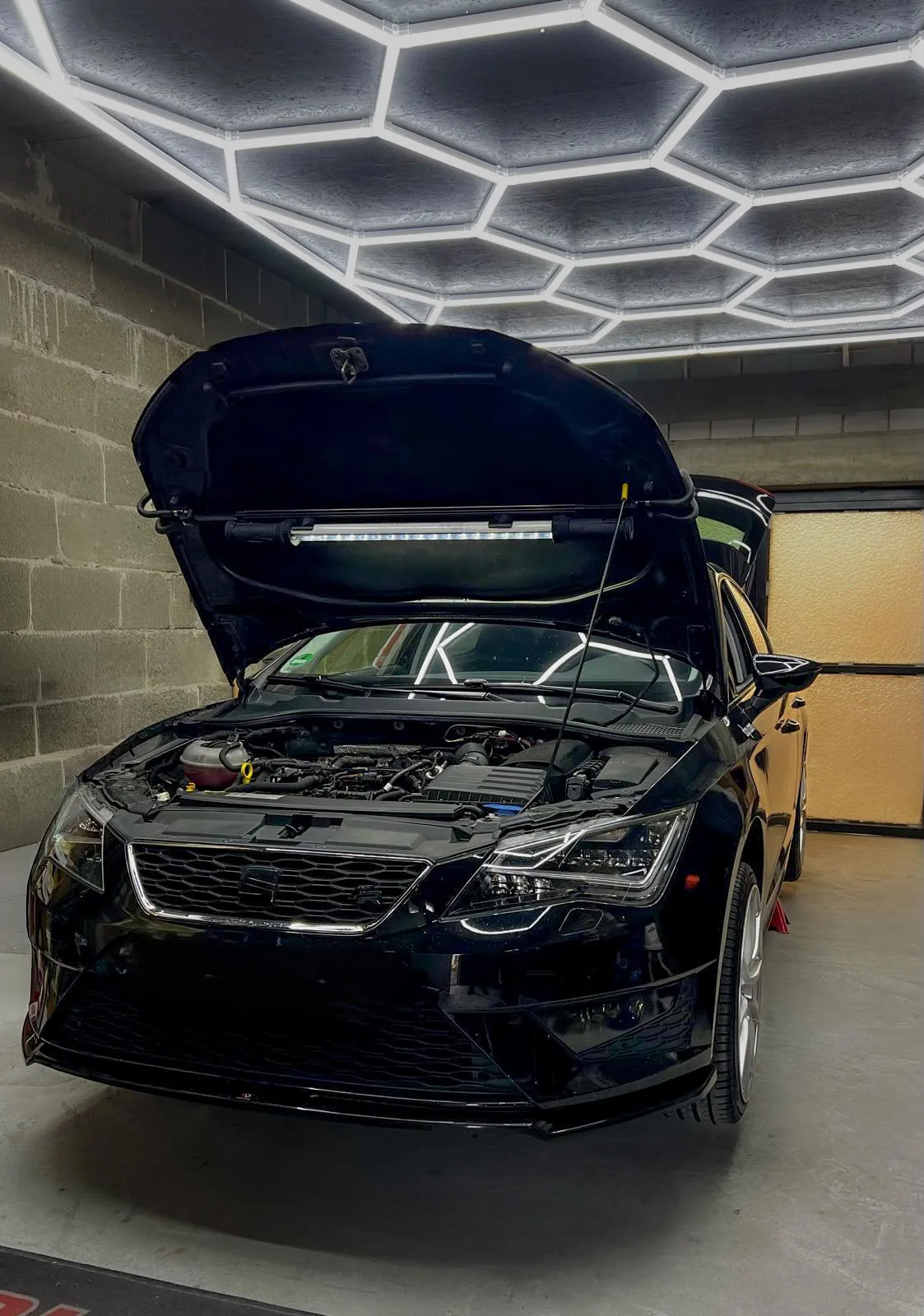 Schwarzer Seat Leon mit geöffneter Motorhaube und Arbeitsleuchte unter der LED-Wabenbeleuchtung